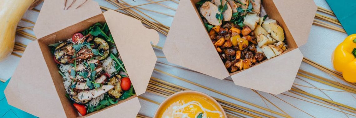 Top view of healthy takeout boxes with salad and soup on a colorful background.